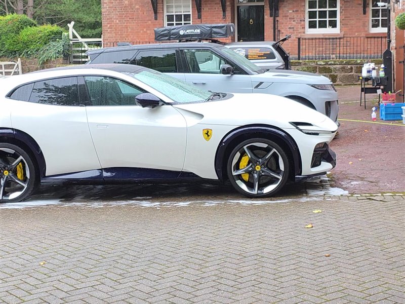 White Ferrari Purosangue after a maintenance valet, side profile on a block-paved driveway